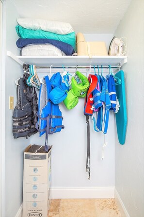 A closet with various life jackets and bags hanging on a rod, a box of packing cubes, and a shelf with folded clothes. - ON Siesta Key BEACH! Pool,Remodeled! 2bd2ba, sleeps 6, 3mins from door to sand   (Sarasota)