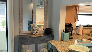 A kitchen with a granite countertop, a dining table, chairs, a decorative mirror, and a sign above the mirror.