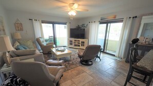 A spacious living room with a ceiling fan, a television, and a sliding glass door leading to a balcony.