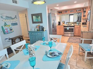 A dining area with a table set for four, surrounded by white chairs with blue cushions. A glass vase with seashells is on the table. - ON Siesta Key BEACH! Pool,Remodeled! 2bd2ba, sleeps 6, 3mins from door to sand   (Sarasota)