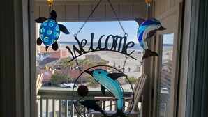Une pancarte « Bienvenue » ornée de motifs décoratifs représentant des tortues de mer et des dauphins, placée sur un balcon donnant sur une plage.
