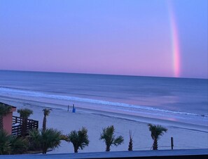 A beach with a clear view of the ocean and a rainbow in the sky.
