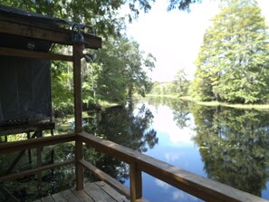 Een houten terras met uitzicht op een rustig meer, met bomen weerspiegeld in het water.
