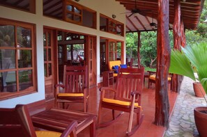 A covered outdoor seating area with wooden furniture and a stone floor.