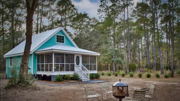 A turquoise house with a porch, surrounded by a forest.