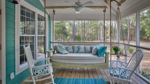 A porch with a swing seat, rocking chairs, and a view of the forest.