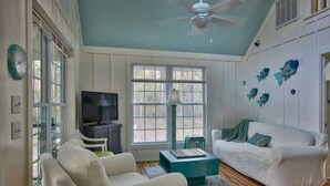 A living room with a white sofa, a teal coffee table, and a TV on a stand.