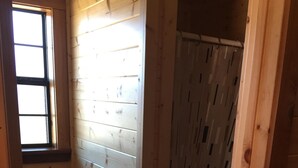 A wooden cabin bathroom with a toilet, a shower curtain, and a window. - Crooked Creek Ranch Cabin 2 (Hamilton)