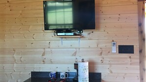 A television mounted on a wooden wall, a coffee maker, and two mugs on a counter. - Crooked Creek Ranch Cabin 2 (Hamilton)