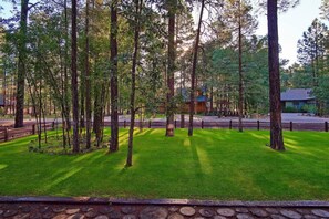 Un área boscosa con un sendero pavimentado, una cerca de madera y un edificio al fondo.