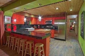 A kitchen with red cabinets, a stainless steel refrigerator, and wooden stools. - Kobey's Ski Lodge - Sleeps 33 - Theater Room - Game Room - Golf - Dogs Welcome (Pinetop)