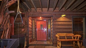 L’intérieur d’une cabane en bois, avec une porte rouge, un banc et une balançoire faite d’une corde.