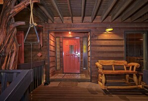 Interior de una cabaña de madera con una puerta roja, un banco y un columpio de cuerda.