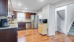 A kitchen with wooden cabinets, stainless steel appliances, a microwave, and a television on a stand. - 🌻Luxury King Beds🌻Nearby Parks🌻 Reserved Parking🌻Smart TVs🌻Google Fiber🌻 (Overland Park)