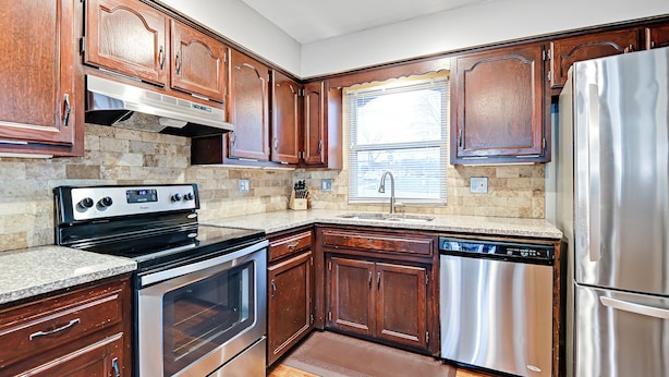 A kitchen with wooden cabinets, stainless steel appliances, a granite countertop, and a window with blinds. - 🌻Luxury King Beds🌻Nearby Parks🌻 Reserved Parking🌻Smart TVs🌻Google Fiber🌻 (Overland Park)