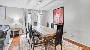 A dining area with a wooden table, chairs, a chandelier, and a painting on the wall. - 🌻Luxury King Beds🌻Nearby Parks🌻 Reserved Parking🌻Smart TVs🌻Google Fiber🌻 (Overland Park)
