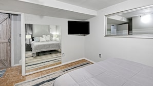 A bedroom with a bed, a television mounted on the wall, a mirror, and a door leading to another room. - 🌻Luxury King Beds🌻Nearby Parks🌻 Reserved Parking🌻Smart TVs🌻Google Fiber🌻 (Overland Park)