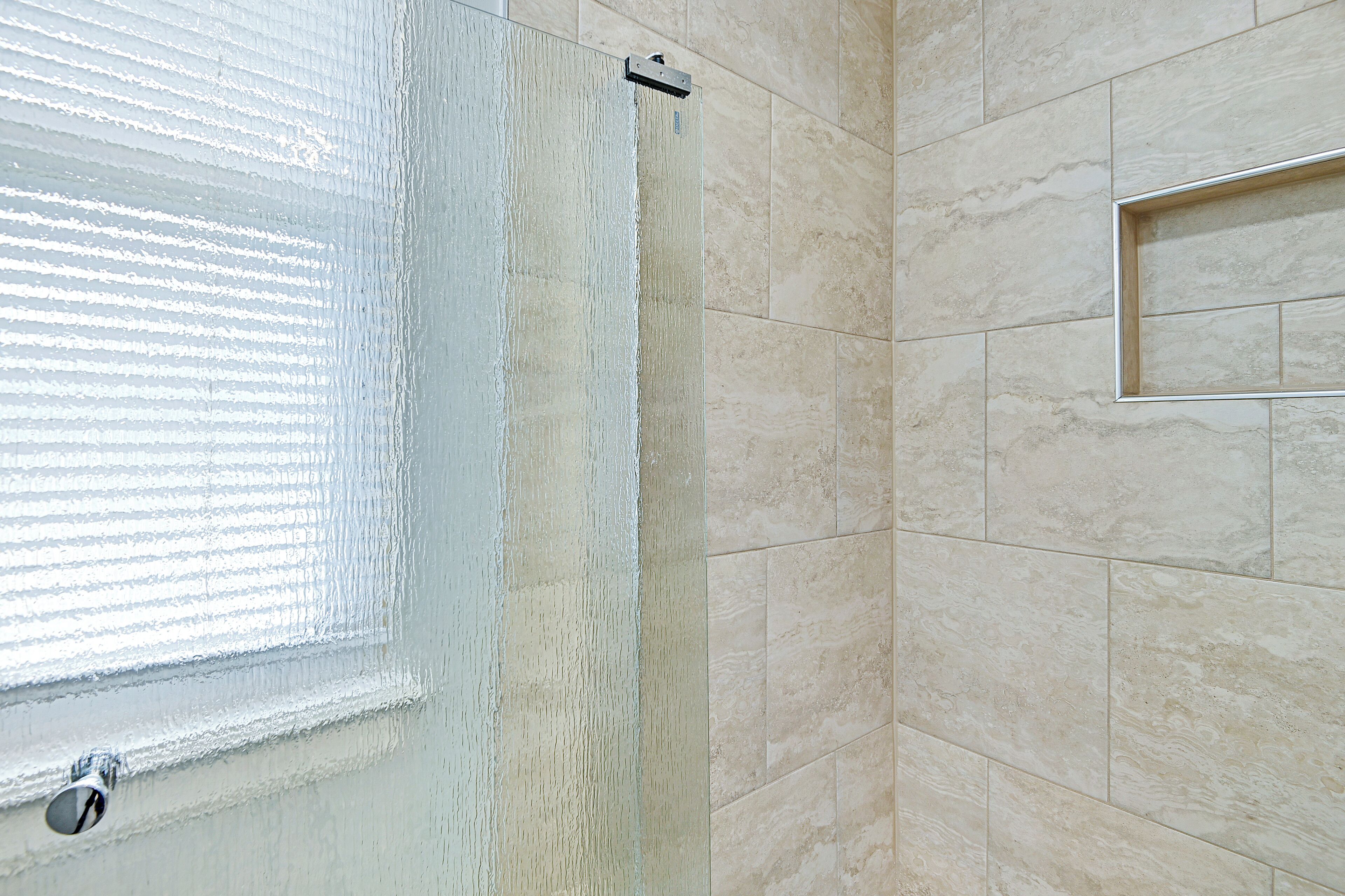 Une salle de bain dotée d’une grande fenêtre, d’un espace douche et de murs recouverts de carreaux de couleur beige.
