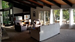 Uma sala de estar espaçosa com parede de pedra, lareira e janelas amplas com vista para o exterior.