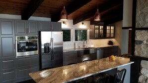 Uma cozinha moderna com eletrodomésticos de aço inoxidável, bancada de mármore e iluminação pendente.