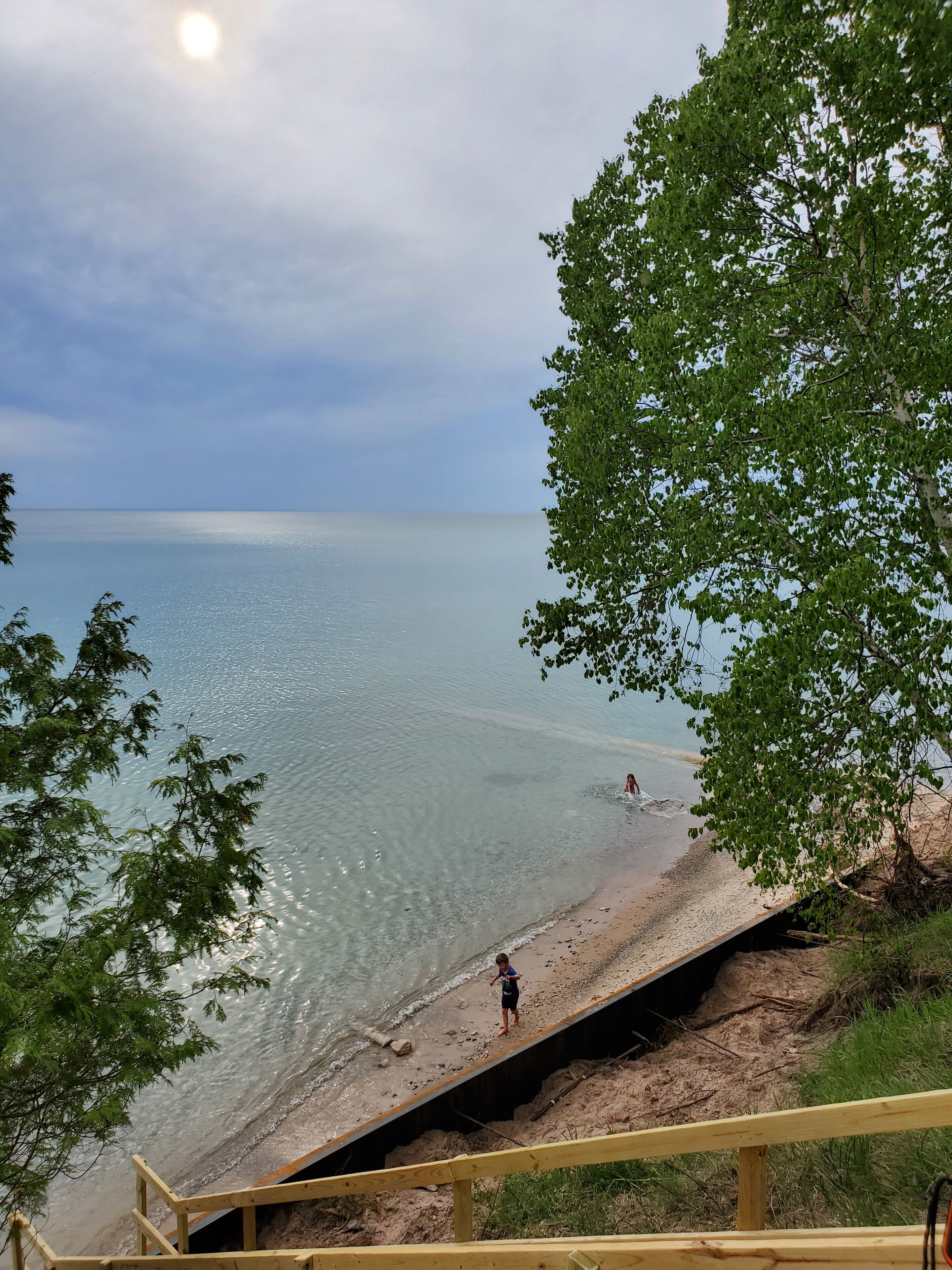 A beach with clear water, a wooden staircase, and a person standing on the sand.