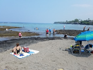 Una playa con gente nadando y caminando por la orilla. Hay toallas y sillas de playa en la arena.