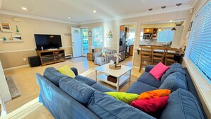 A living room with a large blue sofa, a television, and a dining area with wooden chairs and a kitchen in the background. - Bright and Colorful - Family Friendly!  Short walk to the Best Beaches in Town! (Santa Cruz)
