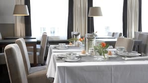 A dining area with a table set for four, chairs, and a view of the city through large windows. - Hotel De Prins (Sittard)