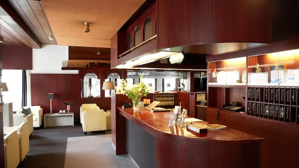 A hotel lobby with a reception desk, seating area, and a view of the dining area. - Hotel De Prins (Sittard)