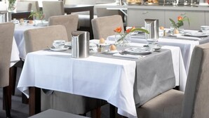 Un comedor con mesas dispuestas para el servicio, una araña y un espejo grande que refleja la habitación.