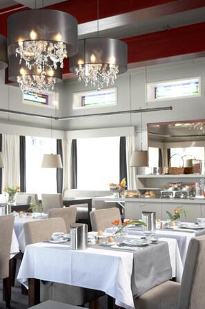 A dining area with tables set for service, a chandelier, and a large mirror reflecting the room. - Hotel De Prins (Sittard)