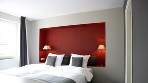 A hotel room with a bed, bedside lamps, a window, and a radiator. - Hotel De Prins (Sittard)