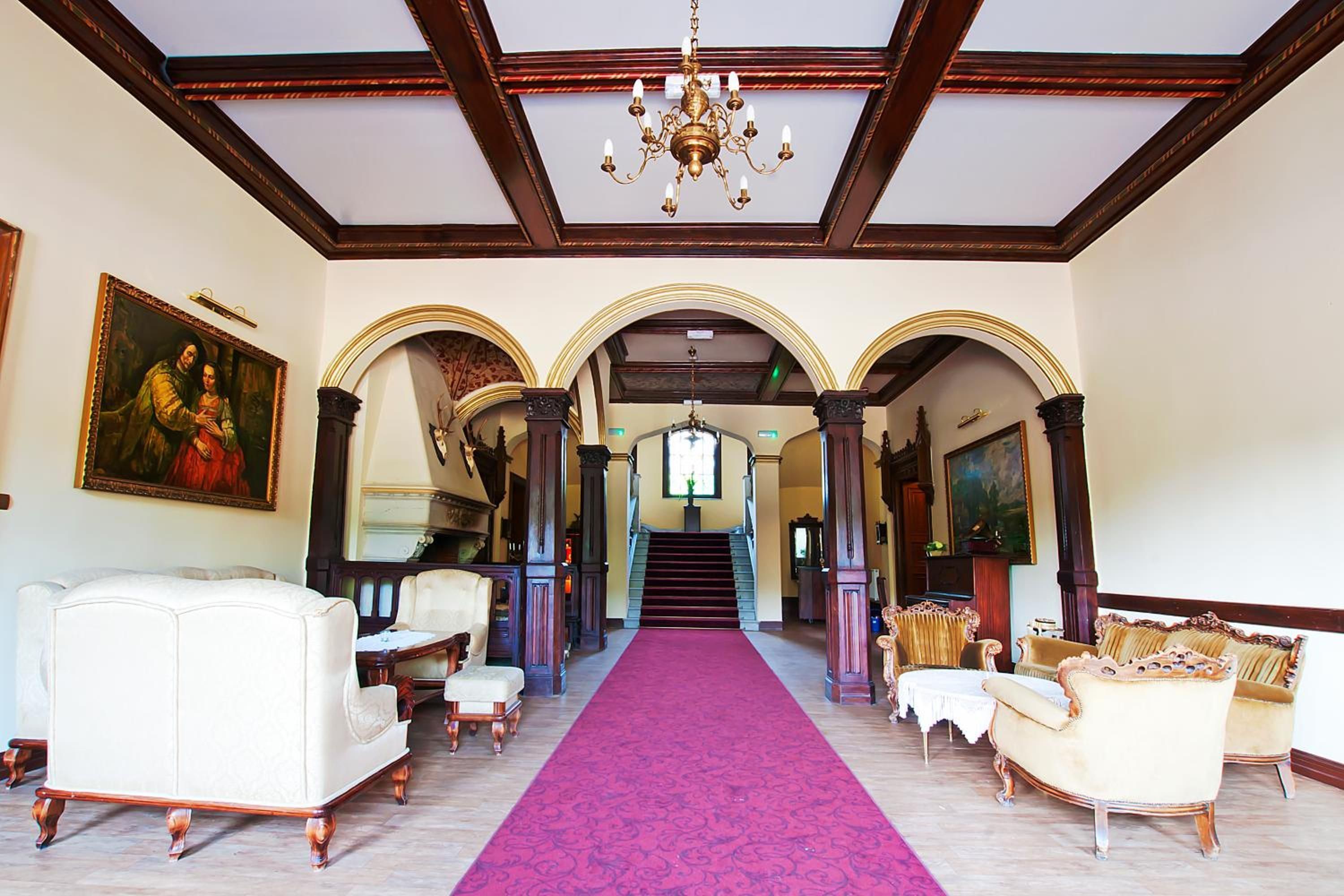 A grand hallway with a red carpet, ornate columns, and classical furniture.
