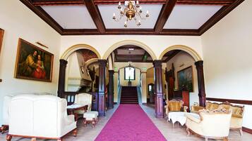 A grand hallway with a red carpet, ornate columns, and classical furniture.