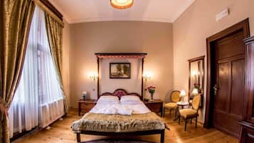 A traditional bedroom with a four-poster bed, a round rug, a wooden floor, a chair, a table, and a door.
