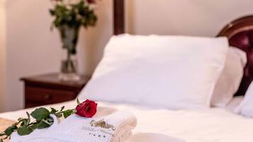 A neatly made bed with white linens and a single red rose on a pillow.