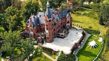 A large, historic building with a central courtyard, surrounded by lush greenery and a well-maintained lawn.