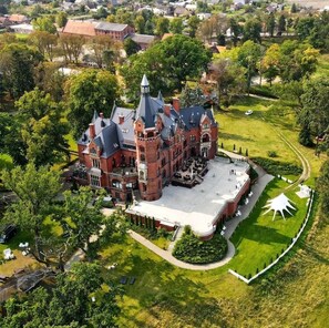 A large, historic building with a central courtyard, surrounded by lush greenery and a well-maintained lawn.