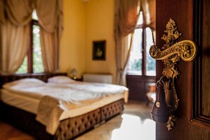 Un dormitorio con cama, una puerta de madera con pomo decorativo y una ventana con cortinas.