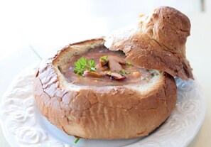 Un bol redondo de pan relleno de sopa y adornado con perejil, sobre un plato blanco.