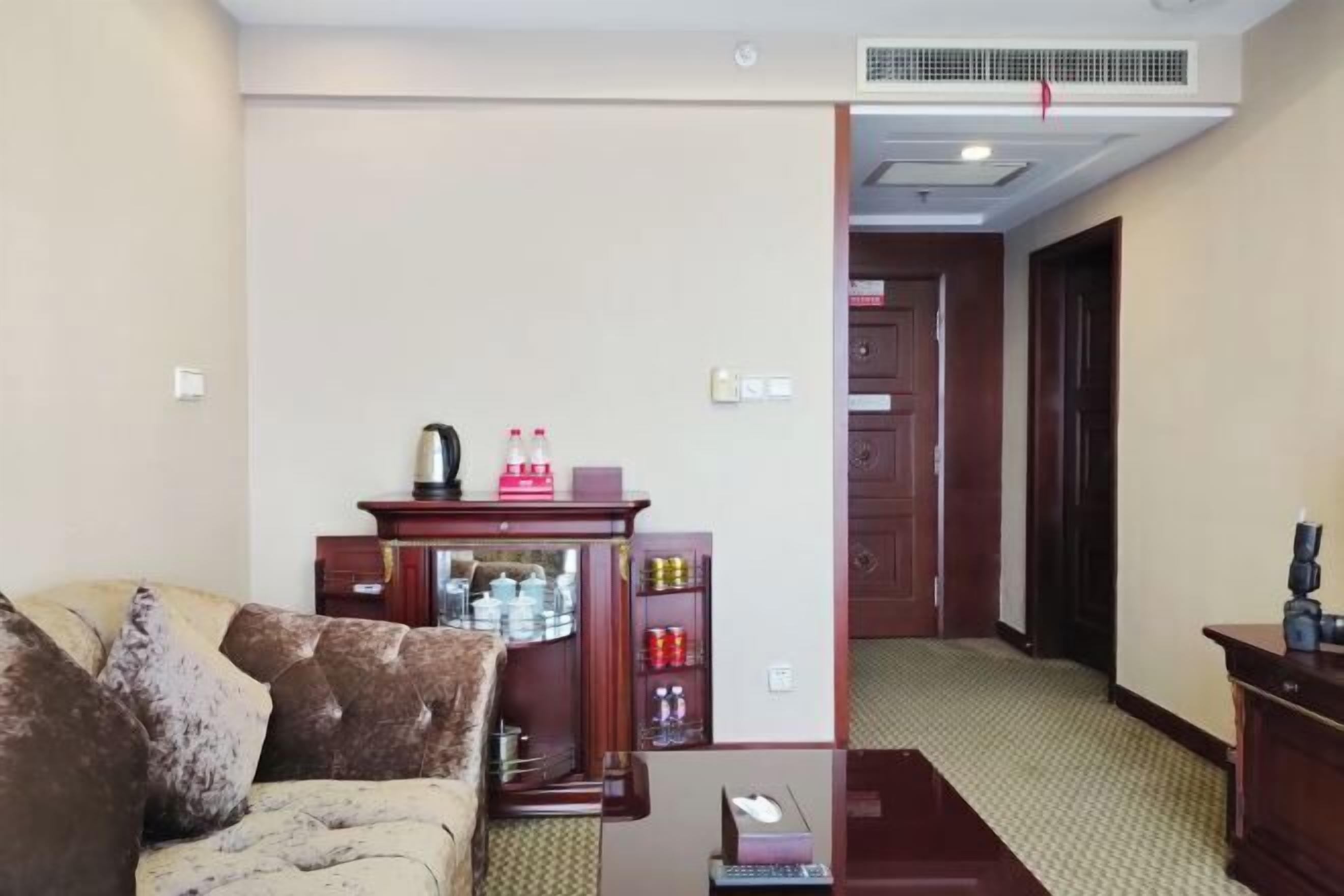 Una sala de estar con un sofá, un mueble de madera con diversos objetos, y un pasillo que conduce a una puerta.