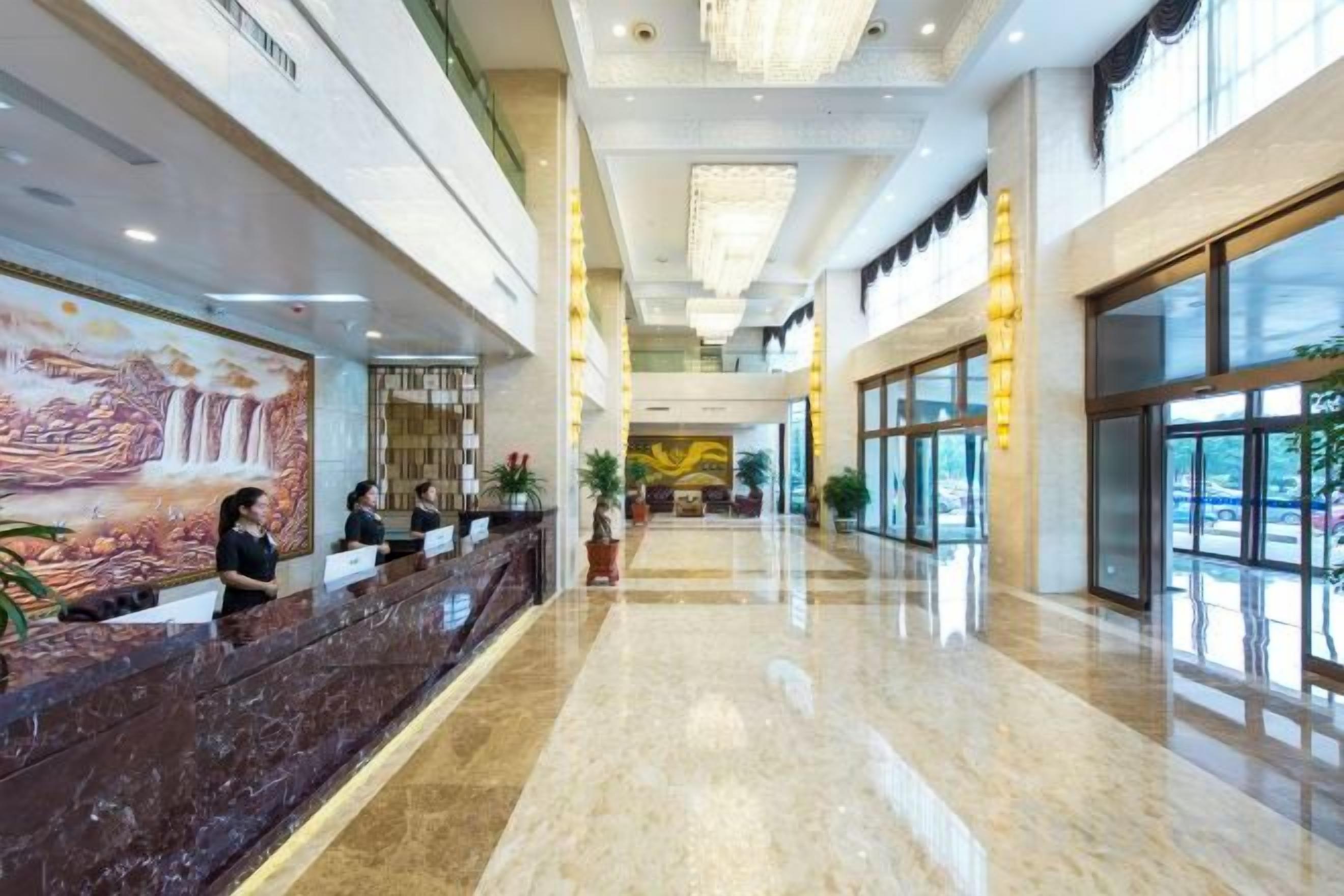 Vestíbulo de hotel con mostrador de recepción, un mural grande y un área espaciosa con techo alto y candelabros.