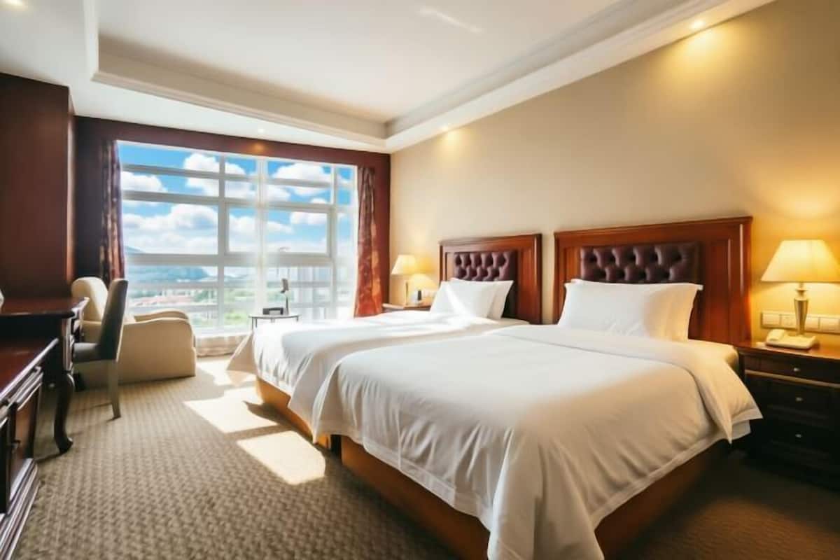 Habitación de hotel con dos camas, un escritorio, una silla y vistas a la ciudad.
