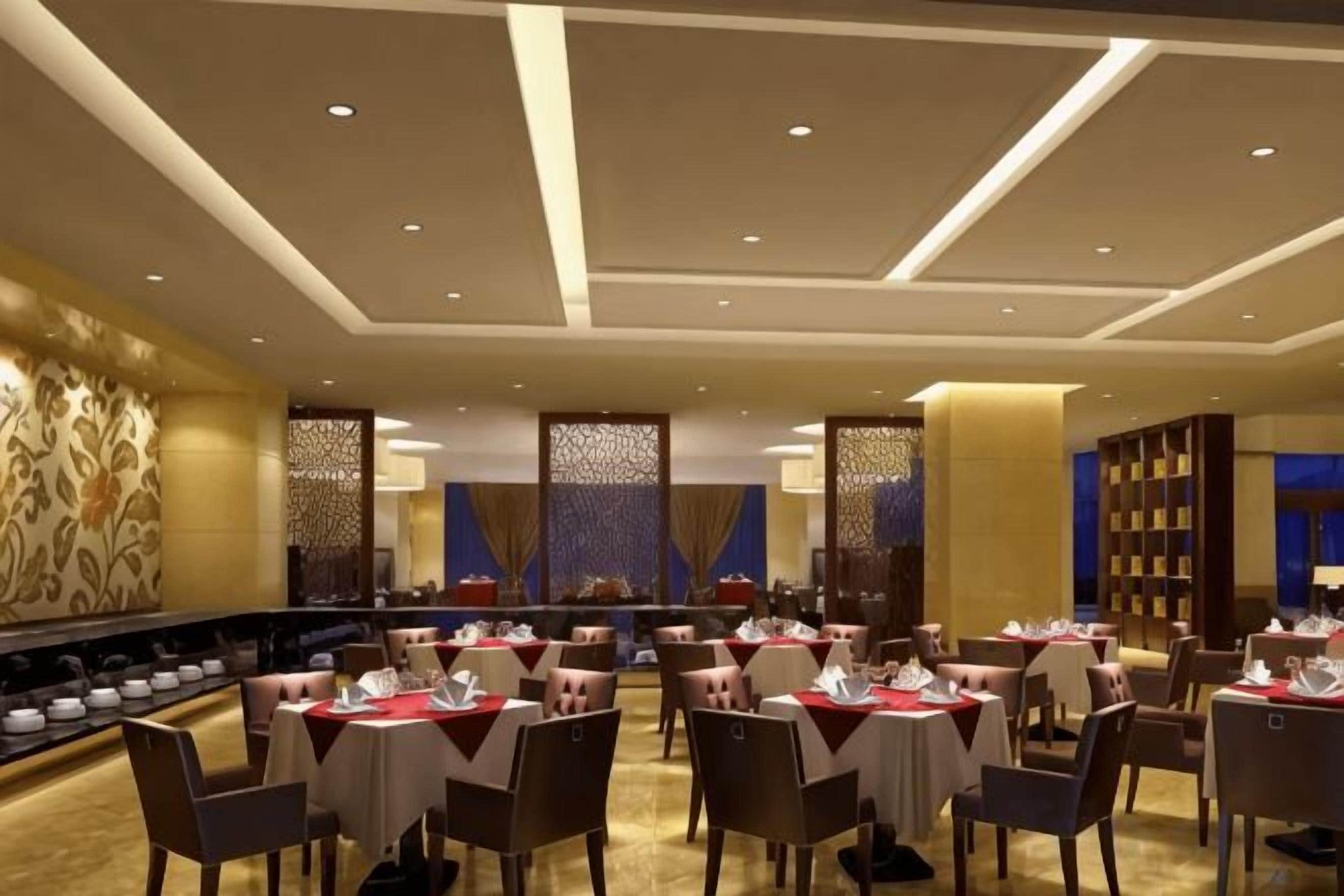 A dining area with tables set for service, a long counter with a display of dishes, and a patterned wall.