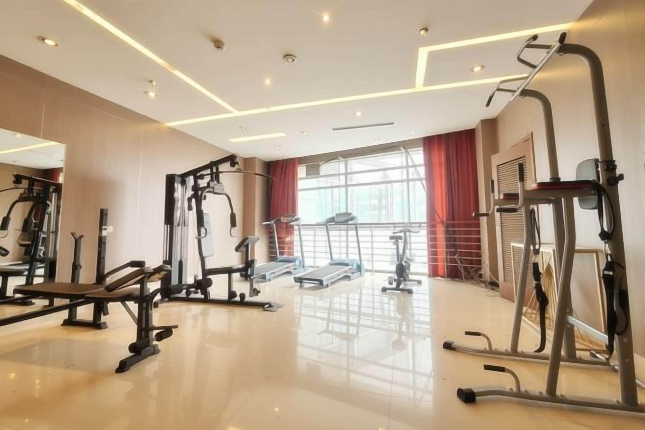 A gym with various exercise equipment, a large window with curtains, and a polished floor.