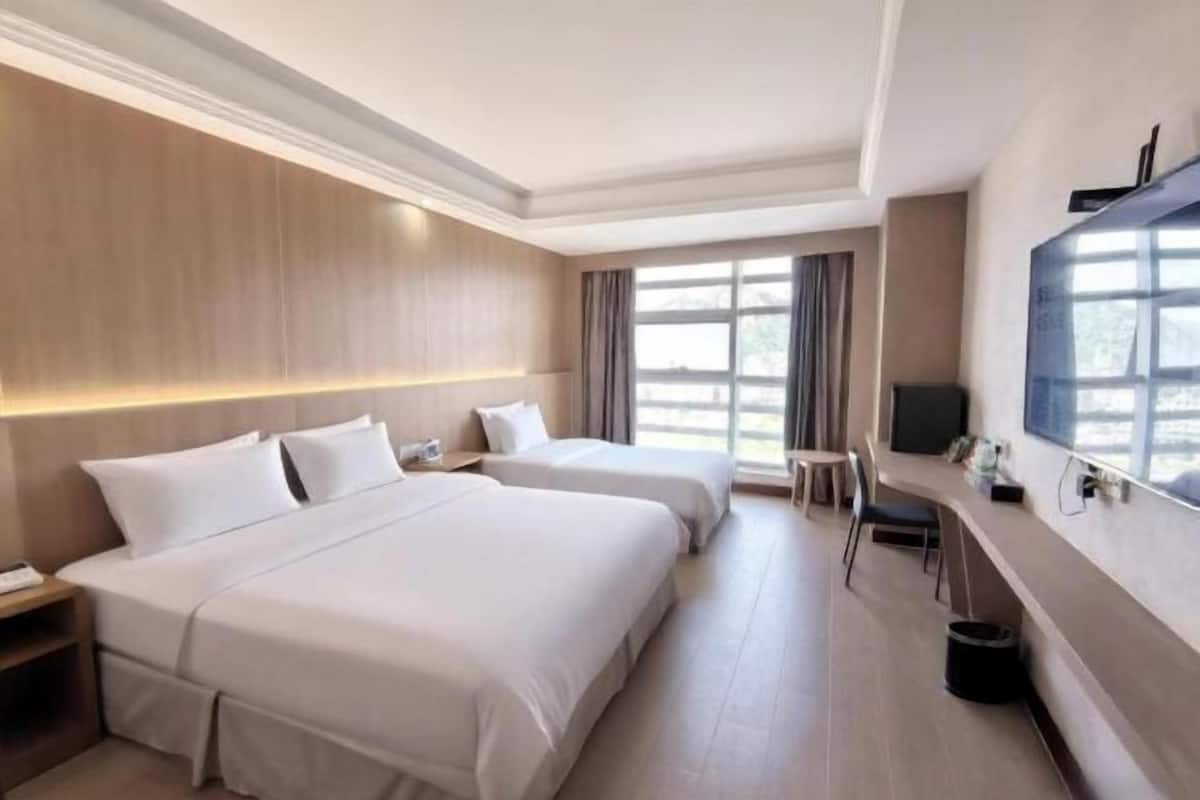 Habitación de hotel con dos camas, un escritorio, una silla, un televisor y ventanas amplias.