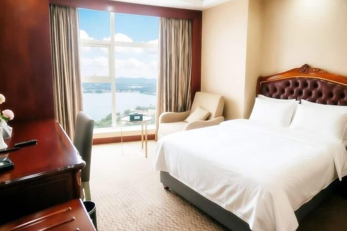 Habitación de hotel con una cama grande, cabecera de madera, escritorio con silla y vistas a una masa de agua a través de amplias ventanas.