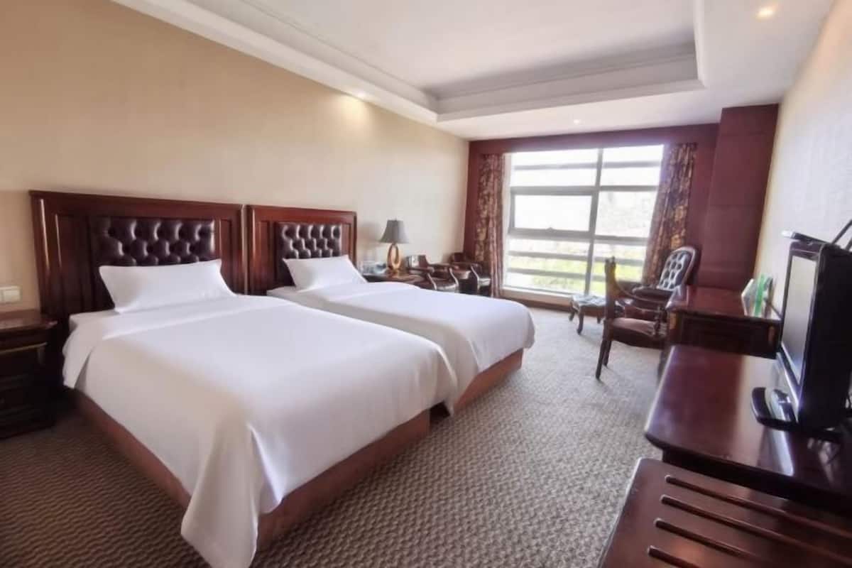 Habitación de hotel con dos camas, un escritorio, una silla y un televisor.
