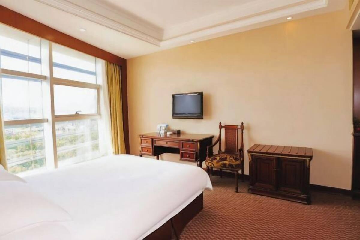 Habitación de hotel con una cama grande, un escritorio con silla, televisión montada en la pared y una ventana con cortinas.