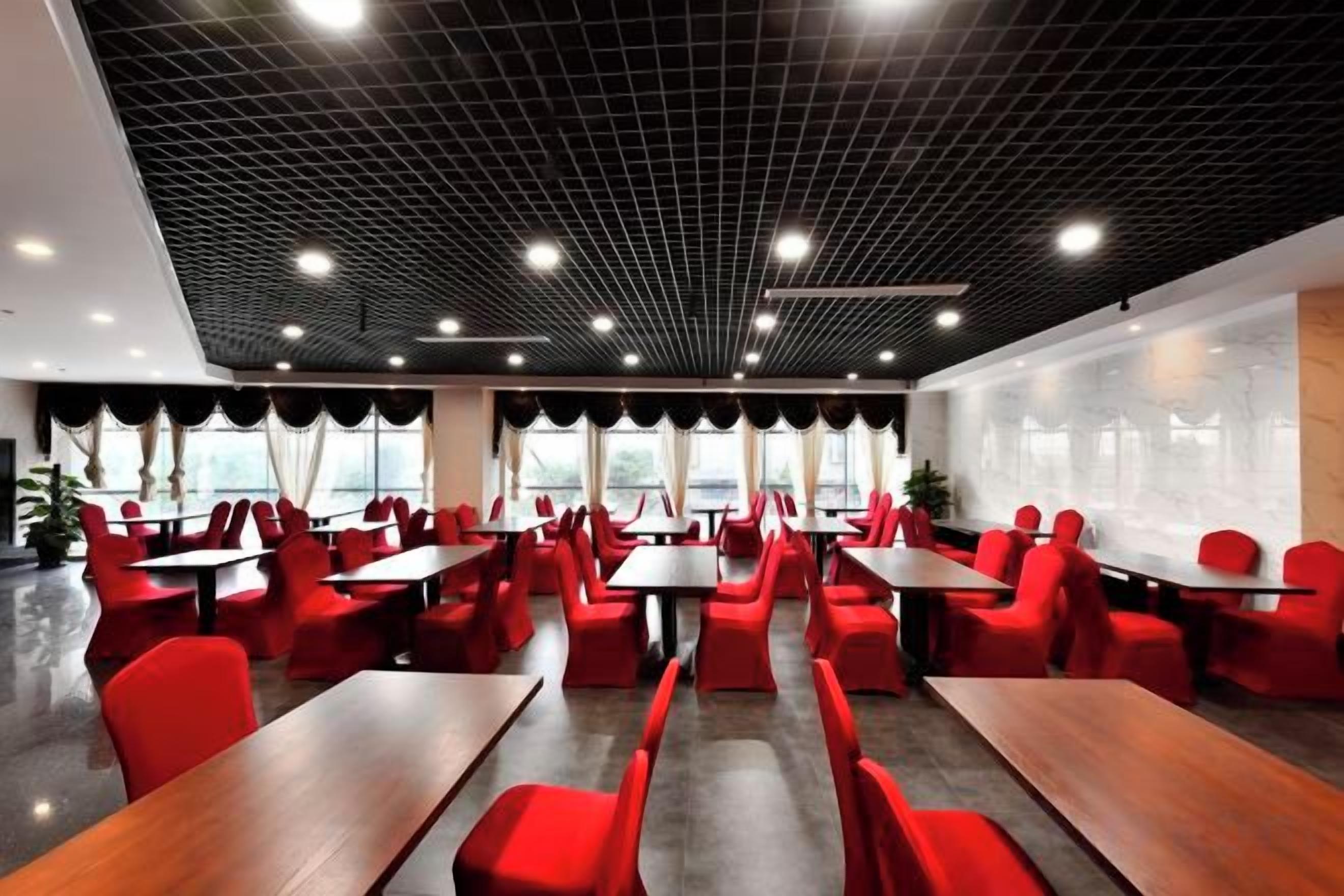 A modern dining area with red chairs and tables, a black ceiling with grid pattern, and large windows.